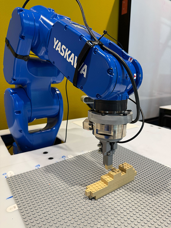 A blue robotic arm builds a figure out of Lego bricks.