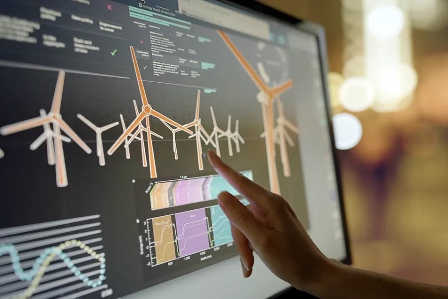 A hand points at images of wind turbines on a computer screen.