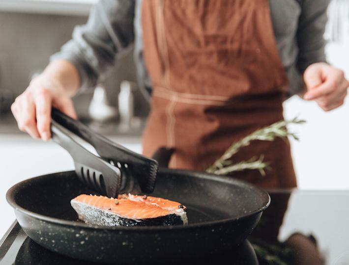 A person wearing an orange apron sautees salmon in a skillet.